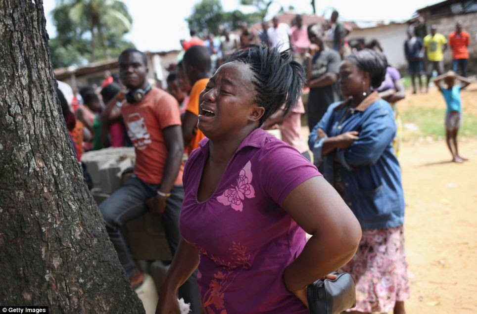 A woman cries as the undertakers, wearing protective clothing go to remove her cousin's body