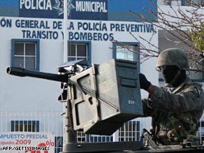 A Mexican soldier guards the entrance at a Cancún police station where the military is investigating a murder.