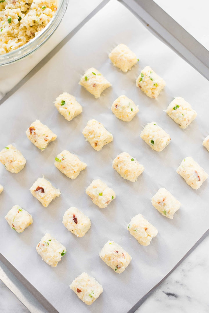 Baking sheet lined with tin foil with the formed cauliflower tots laid out in rows, ready to be placed into the oven and baked.