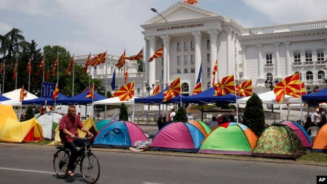 A man on a bicycle passes by tents, posted by the opposition supporters, in front of the government building in Skopje, Macedonia, May 19, 2015.