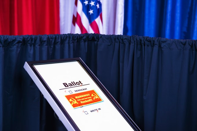 Russians hacked electronic voting machine, showing a red warning window withhammer and sickle icon at a polling station decorated in red, white and blue with an American flag in the background. This is a new form of cyber warfare.