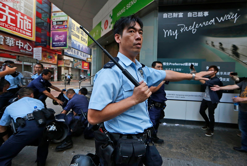 Description of  A police officer holding a police baton secures the area where a pro-democracy protester is being arrested by riot polices in the Mong Kok district of Hong Kong, early Friday, Oct. 17, 2014. Riot police moved in on a Hong Kong pro-democracy protest zone in a dawn raid on Friday, taking down barricades, tents and canopies that have blocked key streets for more than two weeks. (AP Photo/Kin Cheung)