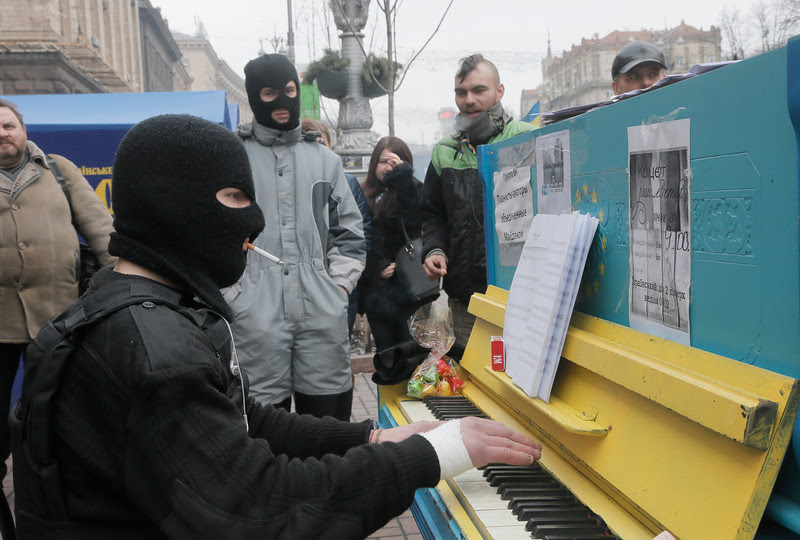Description of  A protester in a balaclava and a flak jacket plays the piano in Kiev's Independence Square, the epicenter of the country's current unrest, Ukraine, Friday, Feb. 14, 2014. A Ukrainian opposition group says that all the protesters detained during nearly three months of opposition demonstrations have been released under an amnesty law. (AP Photo/Efrem Lukatsky)