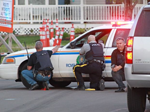 Agentes da polícia se escondem atrás de seus veículos em busca do atirador que teria matado policiais no Canadá (Foto: AP Photo/Moncton Times & Transcript, Ron Ward via The Canadian Press)