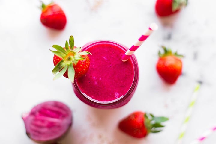 Horizontal view of the beet smoothie topped with a fresh strawberry and raw beet.
