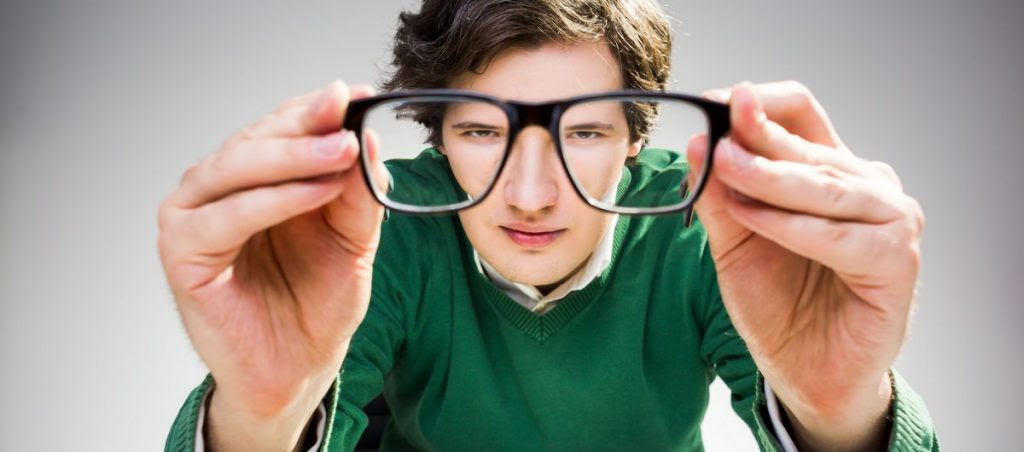 A freelance web developer in green pullover sitting at desk with computer keyboard and looking at the camera through glasses