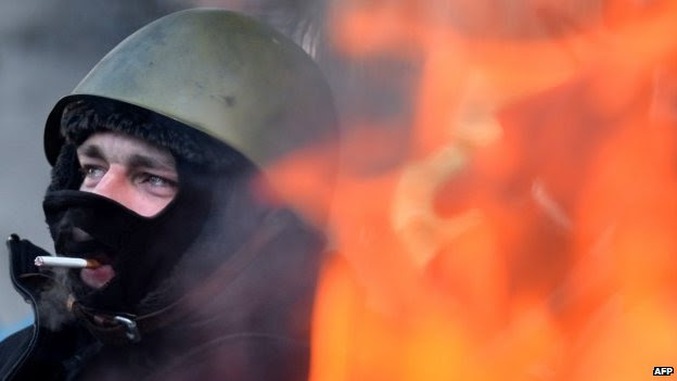 An opposition protester smokes a cigarette as he warms himself near a fire in the centre of Kiev on January 30, 2014