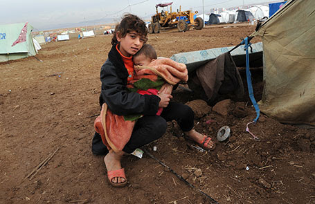 A girl holds a baby on a cold day in a camp for Syrians displaced by civil war