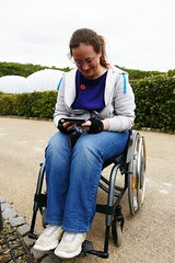 me sitting in my wheelchair, fiddling with my phone, with the Eden biomes in the background