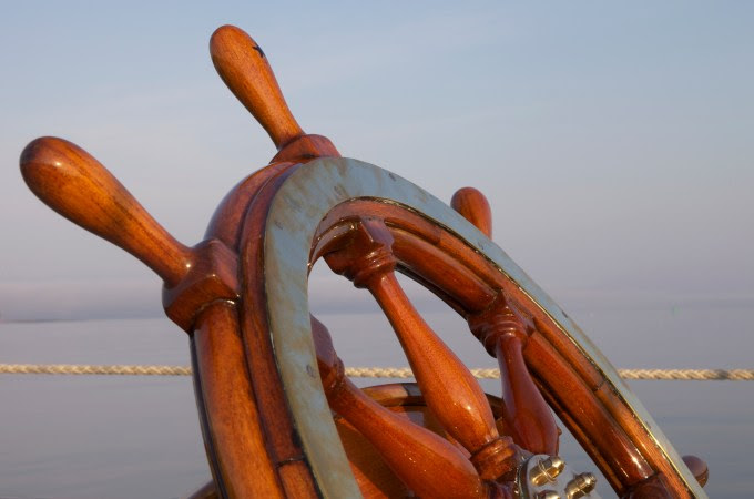 A warm glow highlights the ship's wheel on board the sailing yacht "Sincerity" as sunset approaches.