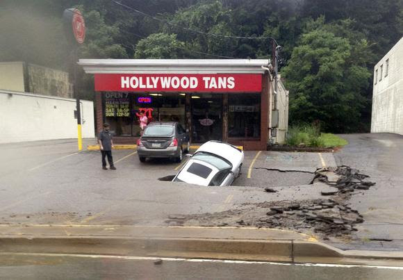 A man looks at a car as it falls into a sinkhole on McKnight Road in Ross Township of Pittsburgh, Pennsylvania, in this handout photo taken August 12, 2014. REUTERS/Roxanne Oglesby/Handout via Reuters