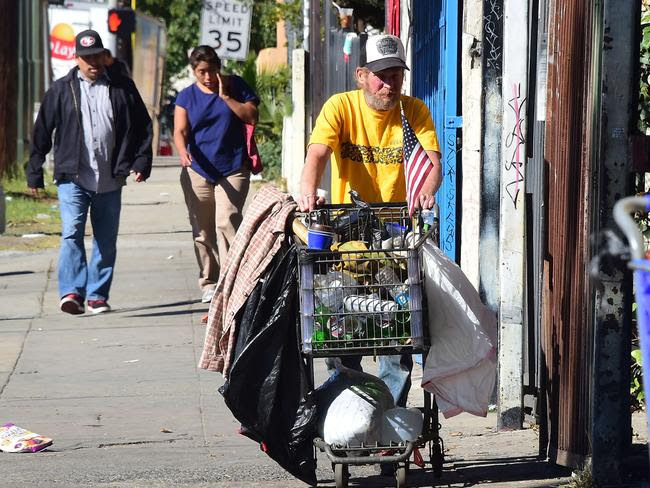 A man pushes a shopping cart full of plastic bottles, blankets and pillows.