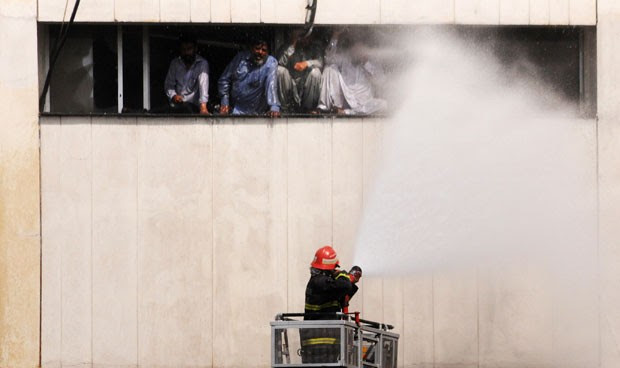 Bombeiro joga água para tentar controlar as chamas e amenizar o calor entre as pessoas encurraladas no prédio (Foto: Arif Ali/AFP)