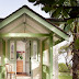 Green Stucco House With White Trim / House with white stucco exterior and arched doorways and windows facing the driveway surrounded by green trees and lawn.