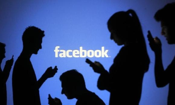 People are silhouetted as they pose with mobile devices in front of a screen projected with a Facebook logo, in this picture illustration taken in Zenica October 29, 2014. REUTERS/Dado Ruvic