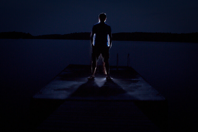 A nighttime portrait of a man on a dock, photographed with central composition