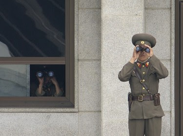 North Korean soldiers look south while on duty in the Joint Security Area, Korean Demilitarized Zone. Image is in the public domain, via Wikipedia.