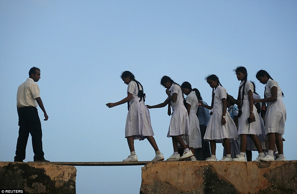 Mind the gap: A group of girls walk across a narrow plank on the walls of the 16th century Galle fort to reach their school in Sri Lanka