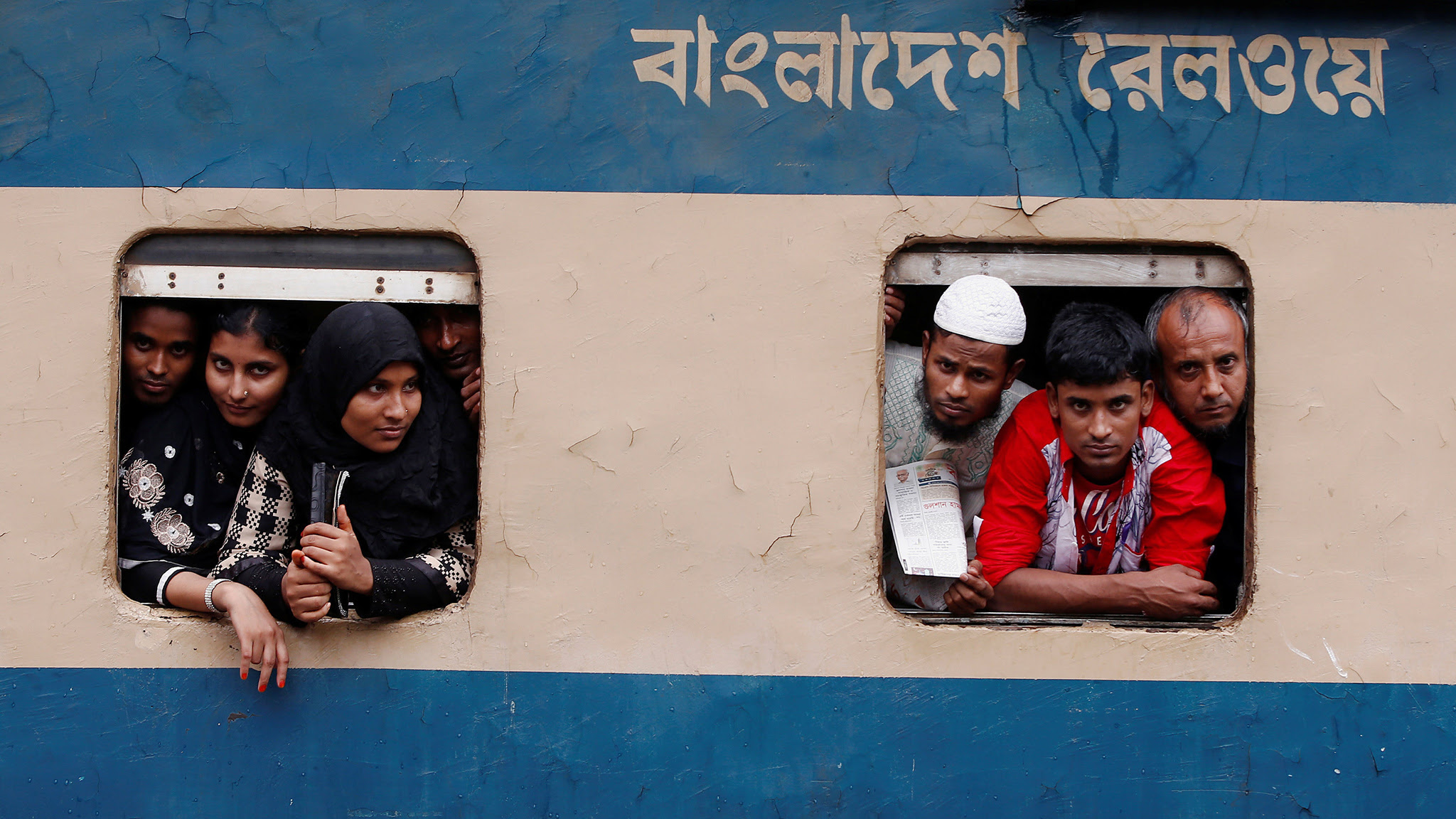 People stand in the windows of an overcrowded passenger train as they travel home to celebrate Eid al-Fitr festival, which marks the end of the Muslim holy fasting month of Ramadan, at a railway station in Dhaka