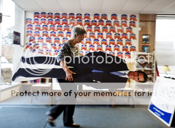 Elderly white woman carries away failed presidential candidate Willard Romney.  Or a cardboard cutout of him.  Hard to say.