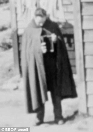 One of the POWs is seen holding the dictionary used to hide the camera as he stands next to one of the barracks