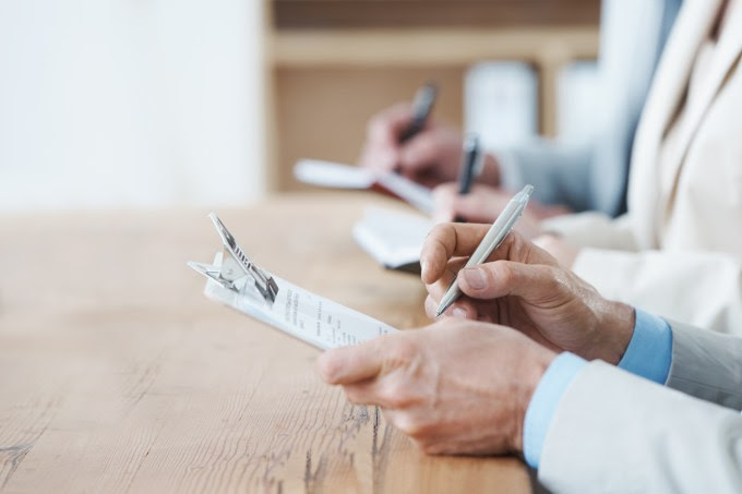 Cropped shot of three coworkers sitting at a table and filling out forms