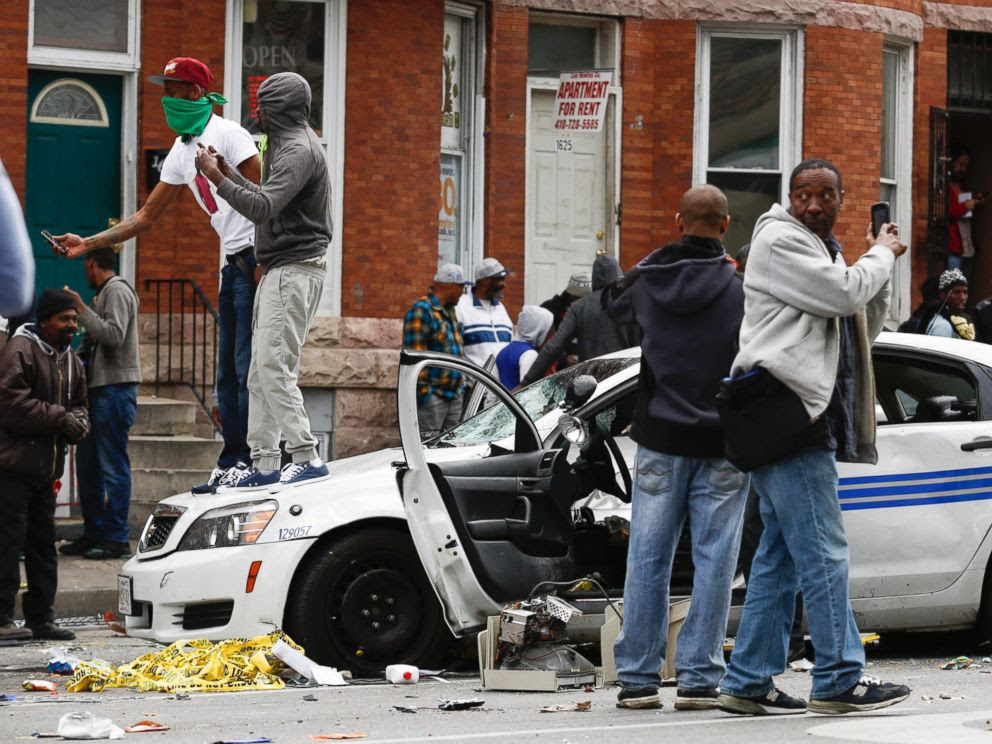 PHOTO: People stand on a damaged Baltimore police car near the intersection of Pennsylvania Avenue and North Avenue on April 27, 2015 in Baltimore, Md.