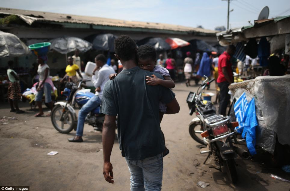 A man carries a child through the streets near an Ebola isolation ward. Ebola, which causes a high fever, bleeding and vomiting, has no cure and no licensed treatment