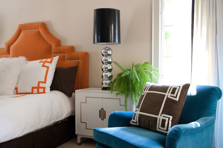 bedrooms - orange headboard nailhead trim blue velvet chair brown pillow white Greek key trim vintage white lacquer Hollywood Regency nightstand polished chrome stacked balls lamps black vinyl lamp shades brown pillows white bedding orange Greek key trim