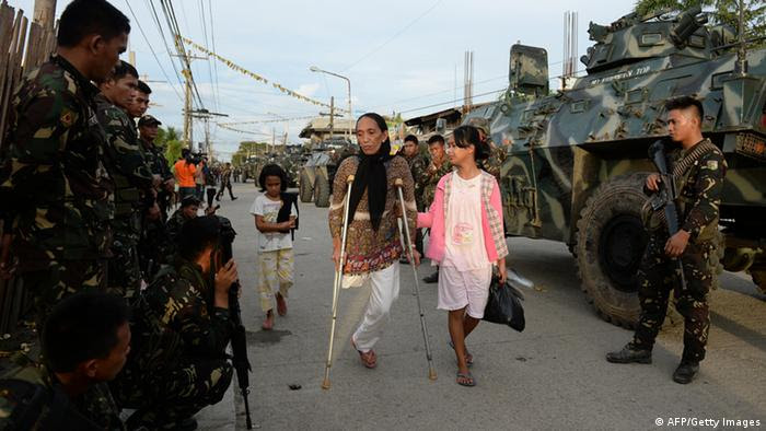 Residents affected by the standoff between rebels and army troops walk past soldiers as they evacuate to a safer area in Zamboanga. Photo: Getty