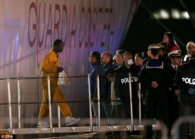 New life: Members of the Italian Police look on as a migrant who survived the ship sinking off the coast of Libya walks the ramp of an Italian Coast Guard's vessel upon arrival at Catania's port yesterday morning