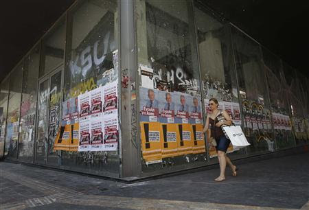 A woman walks past a closed shop with election campaign posters of Democratic Left party and radical left SYRIZA party on it in central Athens June 14, 2012. REUTERS/John Kolesidis