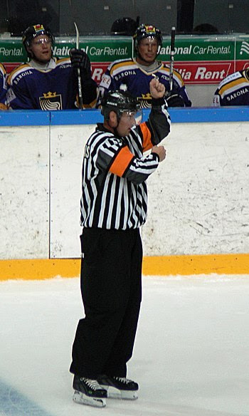 An ice hockey referee signals a penalty for hi...