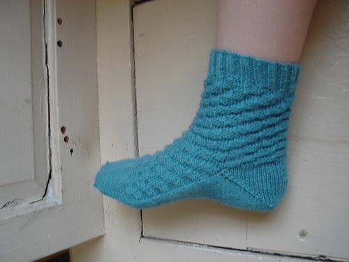 Side view of foot wearing blue-green hand-knitted sock with a checkerboard pattern on the upper
