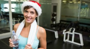 Fit brunette in santa hat smiling at camera at the gym