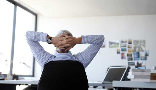 Businessman, aged 52, relaxing at his desk in a modern office.