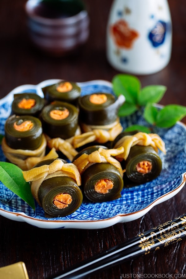 Japanese blue plate containing Salmon Kombu Roll garnished with green leaves.