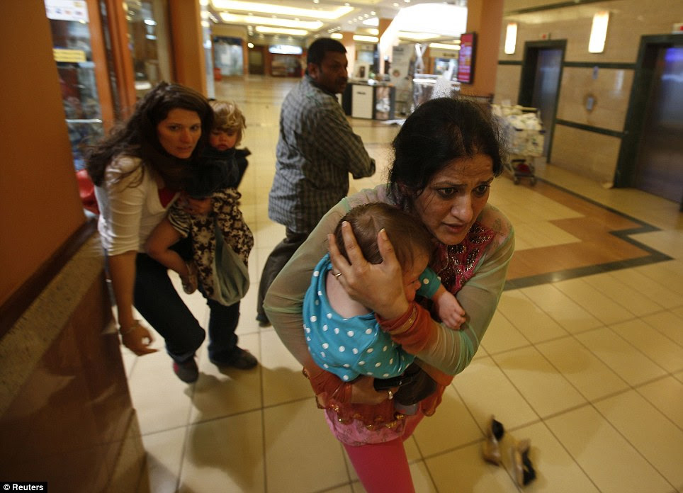 Escape: Women carrying children run for safety as armed police hunt gunmen who went on a shooting spree in Westgate shopping centre