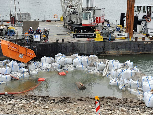 Sacos de areia foram colocados na margem do rio, na tentativa de cercar o artefato militar. (Foto: Harald Tittel/dapd/AP)