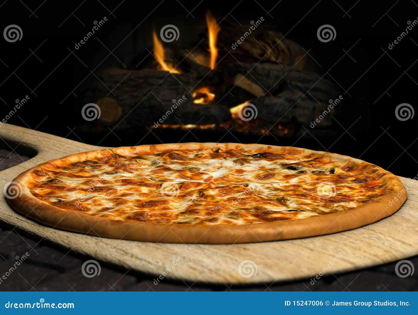 Pizza resting on a pizza peel near an open fire.