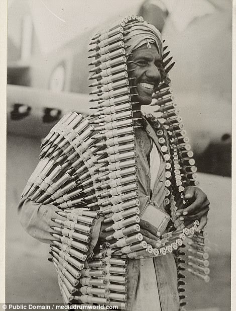 An Arab assistant to an RAF armourer makes a head-dress out of ammunition intended for a Kittyhawk plane