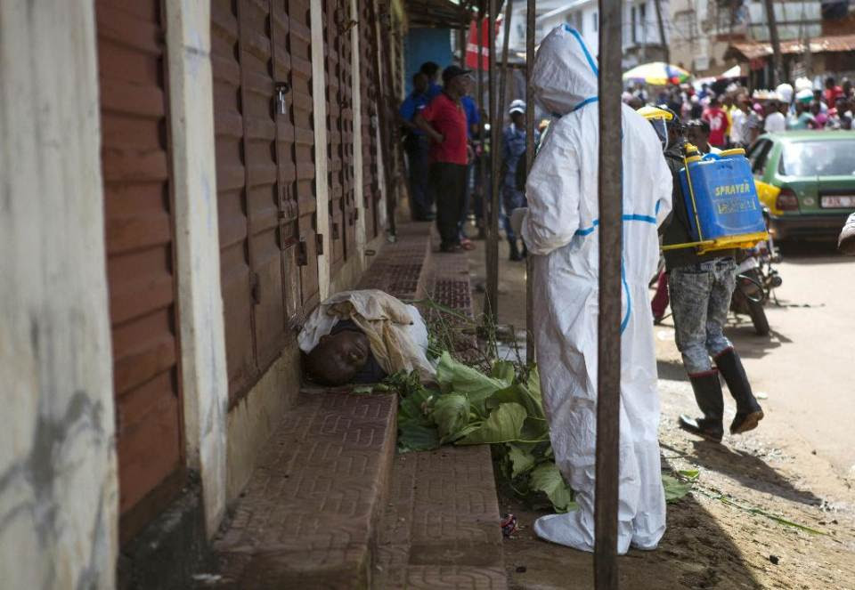Heath workers collect samples from the body of a person suspected to have died from the Ebola virus, as it lies on the street covered in leaves in...