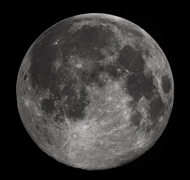 Full moon in the darkness of the night sky. It is patterned with a mix of light-tone regions and darker, irregular blotches, and scattered with varying sizes of impact craters, circles surrounded by out-thrown rays of bright ejecta.