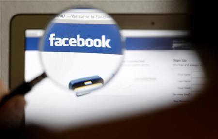In this photo illustration, a Facebook logo on a computer screen is seen through a magnifying glass held by a woman in Bern May 19, 2012. REUTERS/Thomas Hodel