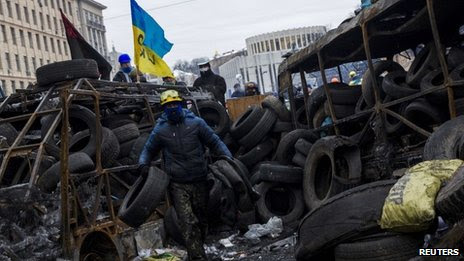 Anti-government protester carries tyres to reinforce barricades built to fend off riot police in Kiev, 28 January 2014