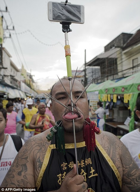 The festival involves a procession that worships abstinence from meat, while mediums also attempt to call on spirits. A man is pictured with spike through his tongue and cheeks, including one which has a mobile phone on the end of it