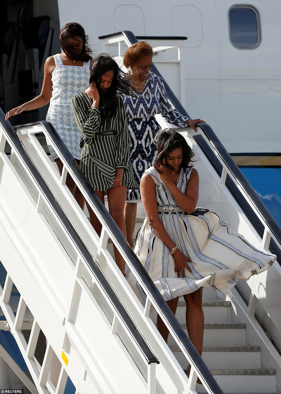 As mulheres Obama - viajando com a mãe de Michelle Marian Robinson - tudo equilibrado segurando seus cabelos e seus vestidos para baixo no vento