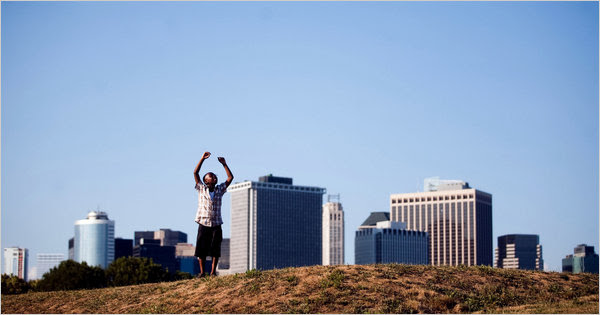 A young visitor to Governors Island stands on the main lawn, with a view of the Manhattan skyline in the background