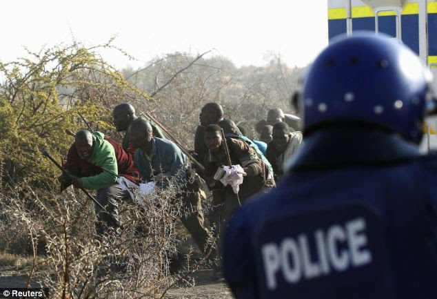 Taking cover: Protesting miners can be seen cowering within the gun sights of an police officer. Witnesses say as many as 18 could have been killed in the shootings