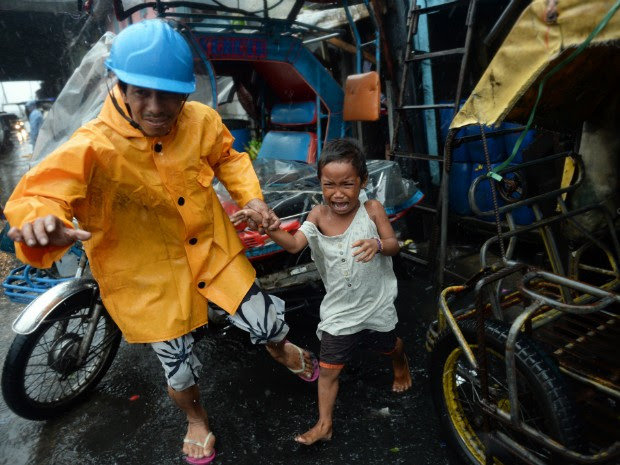 Funcionário de aldeia leva criança durante retirada de famílias em área de risco durante a passagem do tufão nas Filipinas (Foto: Ted Aljibe/AFP)